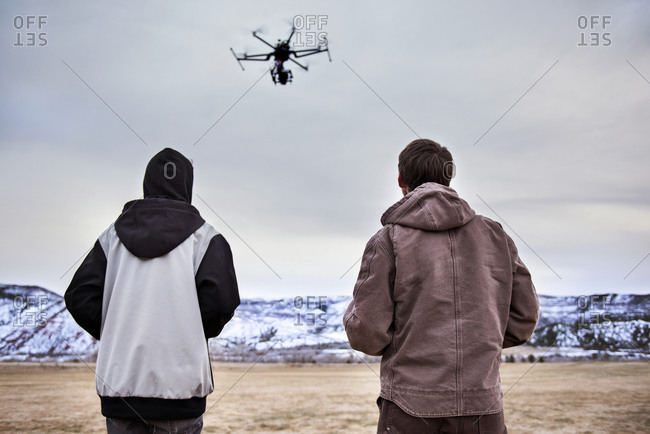 Rear view of father and son flying octocopter on field during winter