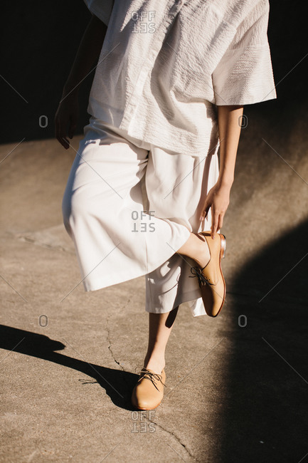 Young woman in oversized white clothing walking touching her shoe