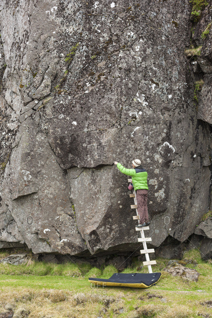 Climber cleaning hand and foot holds before an ascend at Hnappavellir climbing area, Iceland
