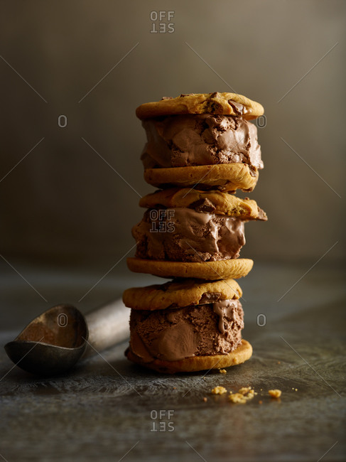 Three chocolate ice cream sandwiches stacked on top of one another with an ice cream scoop