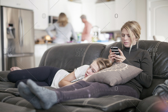A woman checking her phone and a girl lying with her head on a pillow on her lap