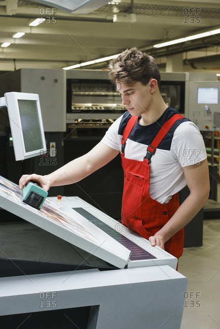 Young worker checking quality of printout with scanner at printing press