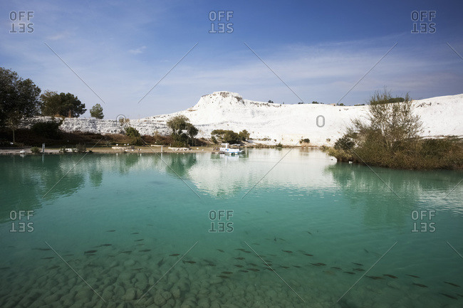 Turquoise water in a pool reflecting a white wall of mineral deposits; Pamukkale, Turkey