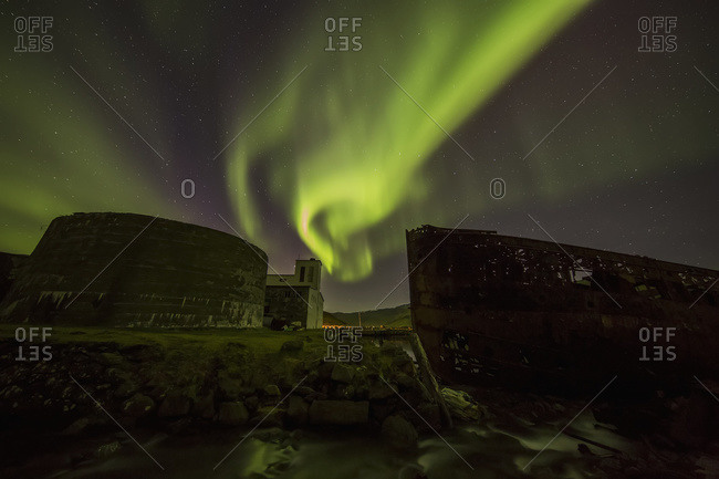 Northern lights over top of the town known as Djupavik along the Strandir Coast, here they are dancing above the old herring factory and shipwreck; Djupavik, Iceland