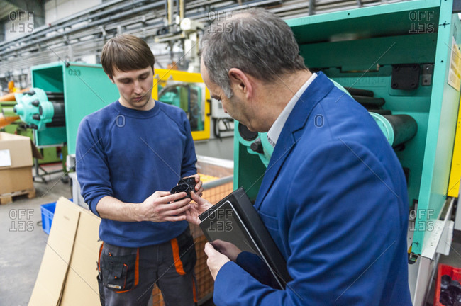 Worker learning about production quality from his manager in a plastics factory