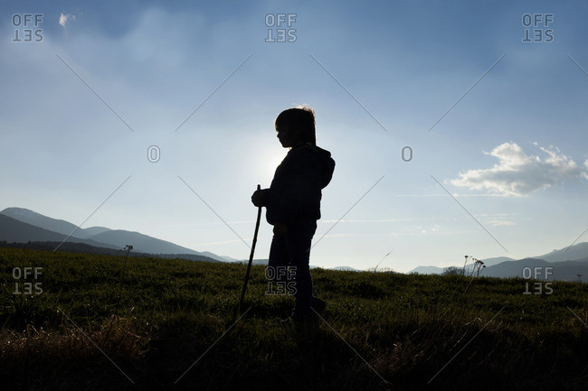 Silhouette of little boy standing on a meadow at backlight