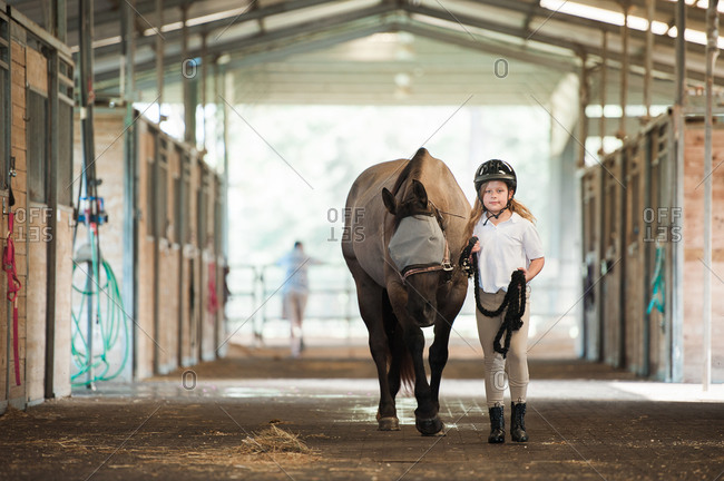 Girl leading a horse through stables