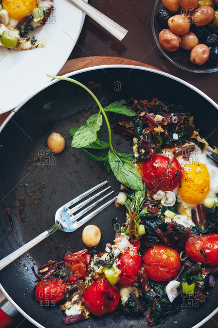 Fried eggs with tomatoes and greens in a frying pan