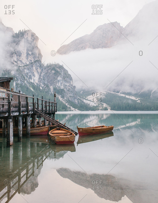 Wood row boats anchored beside a dock on a glassy lake in the Dolomites in Italy