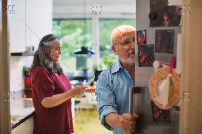 Senior man opening refrigerator while woman using digital tablet at home