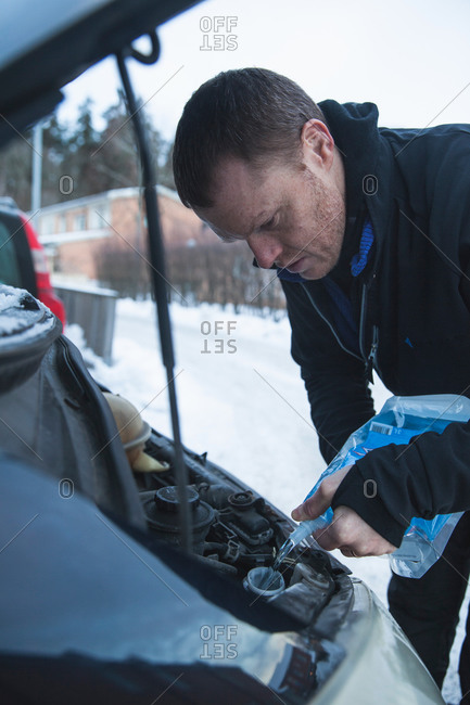 Mature man pouring windshield washer fluid into car during winter