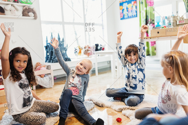 Happy children raising hands while sitting in preschool