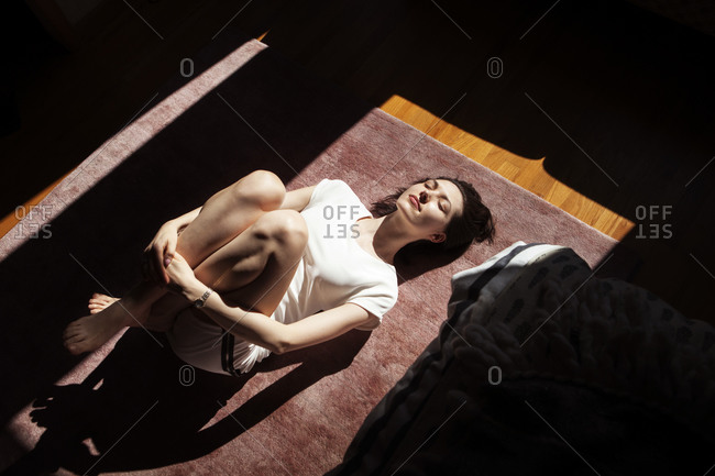 High angle view of woman hugging knees while lying on floor at home