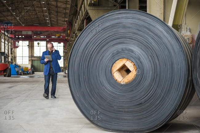 Manager with digital tablet in factory hall with rolls of rubber