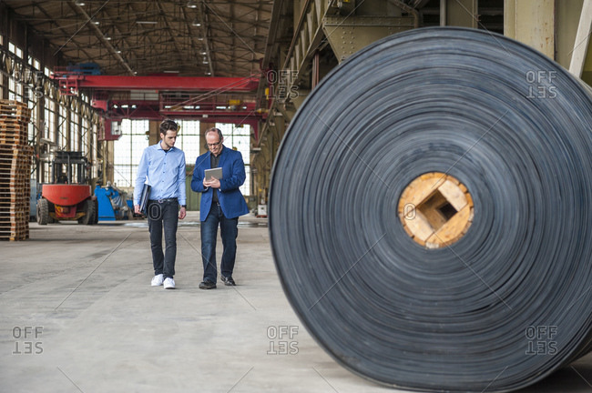 Two men walking in factory hall with rolls of rubber