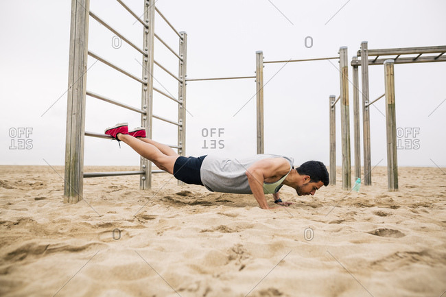 Young man doing push-ups on wall bars on the beach