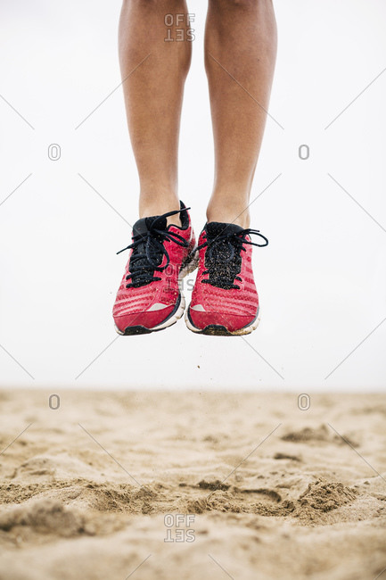 Legs of athlete jumping mid-air in sand