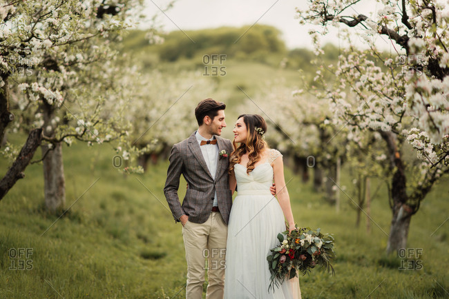 Newlyweds standing in an orchard with arms around each other