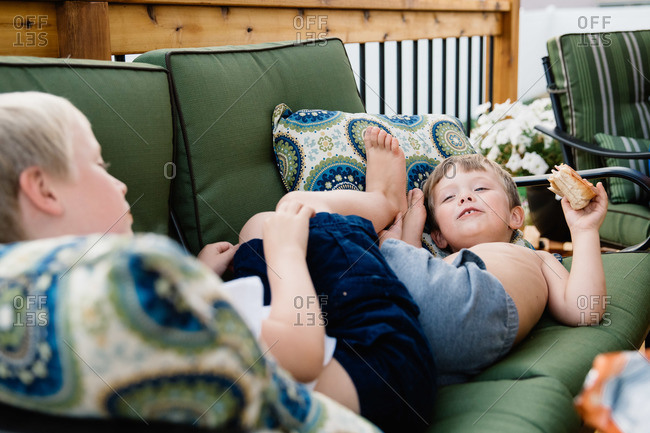 Two boys lying down on the couch together and roughhousing