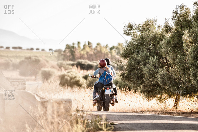 Rear view of mid adult couple riding motorcycle on dusty rural road