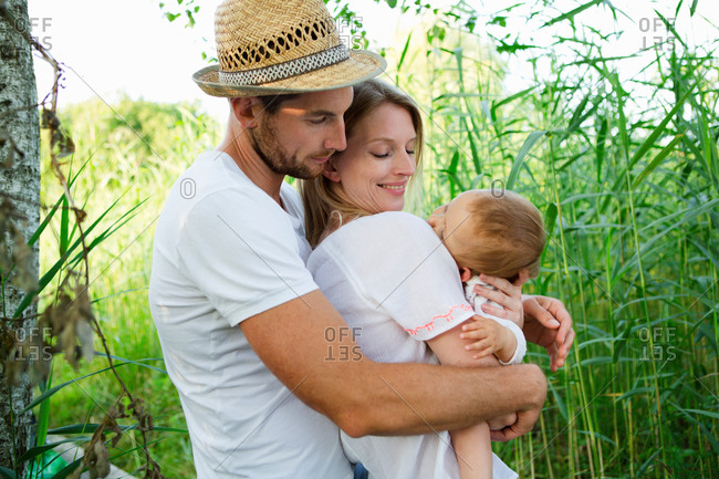 Mid adult couple and baby daughter with arms around each other in reeds