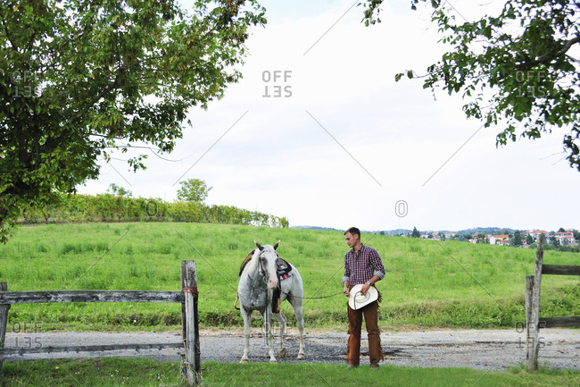 Young man in cowboy gear leading horse through gateway