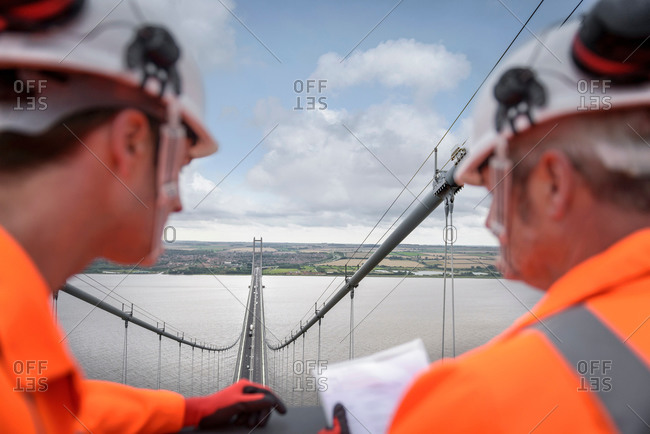 Bridge workers looking down from top of suspension bridge