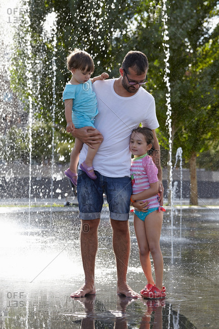 Father and two daughters playing in water fountains, Madrid, Spain