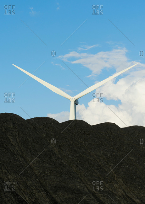 A wind turbine located behind a pile of coal, that waits to be burned in the nearby power station