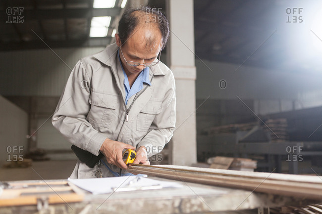 Carpenter using a tape measure to measure a wood plank with  in factory, Jiangsu, China
