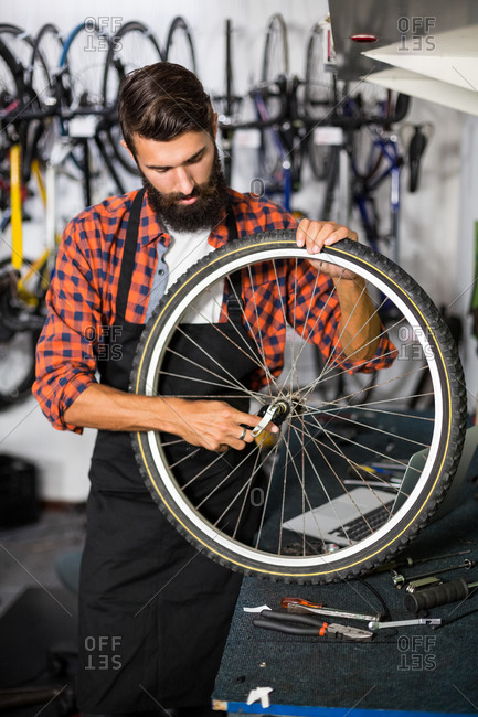 Hipster bike mechanic holding a bike wheel in bike repair shop
