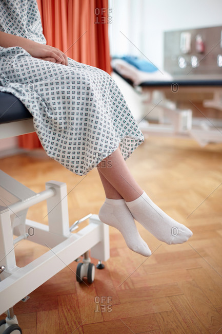 Girl sitting on hospital bed, wearing examination gown