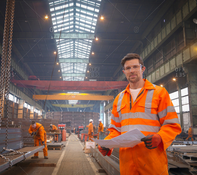 Engineer holding plans in marine fabrication factory, portrait