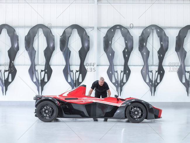 Engineer inspects supercar in factory with carbon fiber car body shells hanging on wall