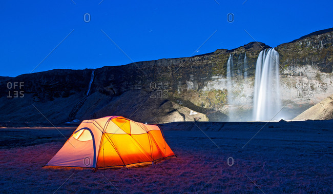 Illuminated tent and Seljalandsfoss waterfall at night, South Iceland