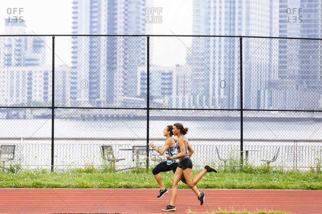 Two women sprinting on a track with a city skyline in the background