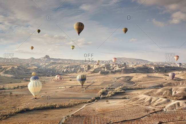 Large group of balloons landing on warm brown fields at sunrise In the distance are ancient canyon walls and rock formations