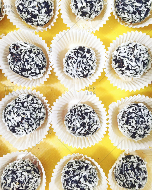 An overhead close up of a gluten-free chocolate truffles with shredded coconut in white wrappers on a yellow tray