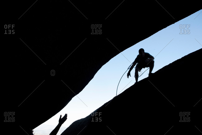 Silhouette of young male climbers reaching out for each other on rock