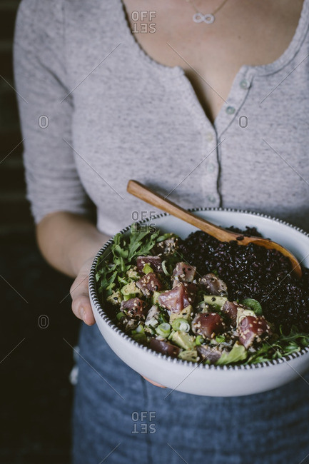 Woman carrying a bowl filled with sesame crusted seared tuna salad and forbidden rice