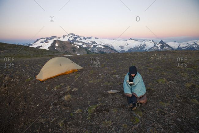 A young woman reads a book while camping on Panorama Ridge in Garibaldi Provincial Park, British Columbia, Canada