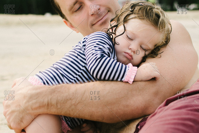 Father holding sleepy little girl on a beach