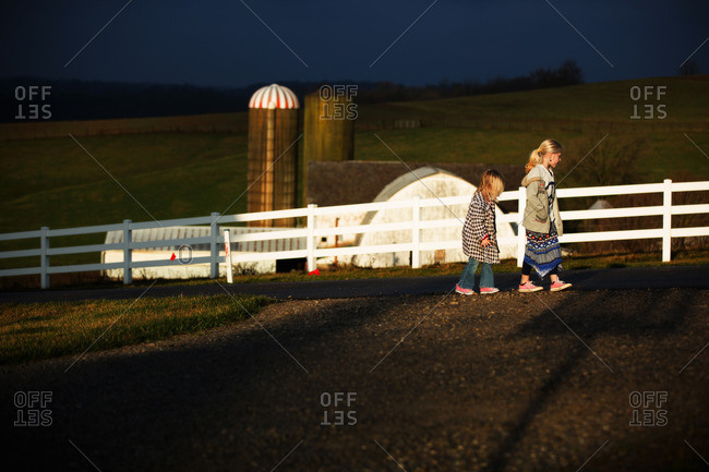 Two girls walking on a road by a farm
