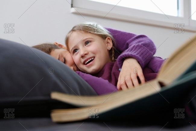 Surface level view of girl lying down on sofa with book, hugging and smiling