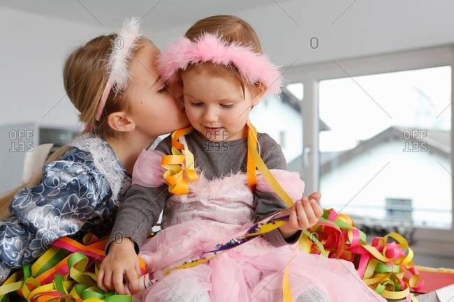 Sisters dressed up as princesses, covered in party streamers, kiss on cheek