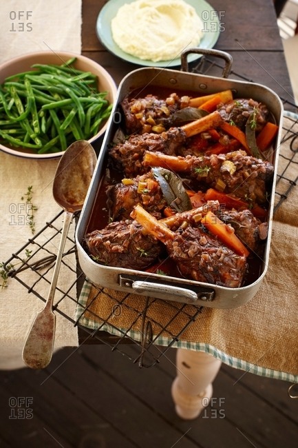 Overhead view of lamb shank stew in roasting tin with green beans and mashed potato