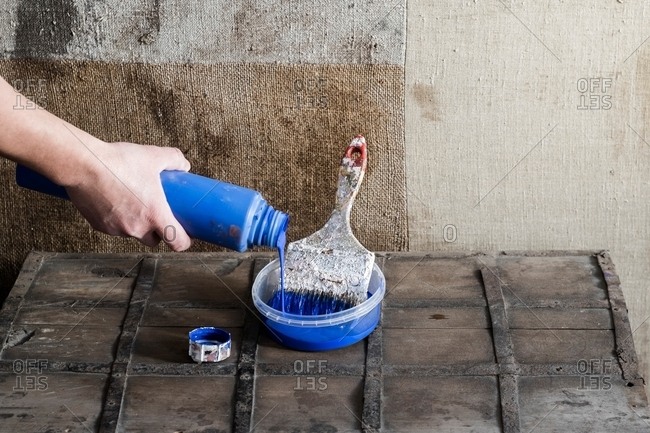 Hand pouring paint into plastic container with paint brush