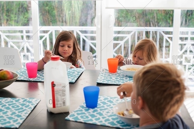 Siblings at dining table eating breakfast