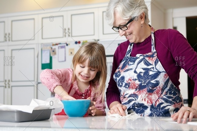 Girl and grandmother mixing cake in bowl at kitchen counter