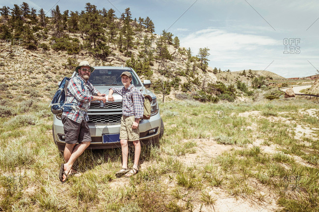 Portrait of man and teenage son on hiking road trip leaning on car hood in landscape, Bridger, Montana, USA